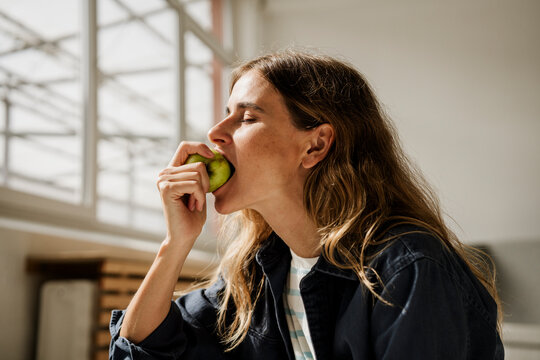 Woman enjoying fresh apple in sunny studio environment