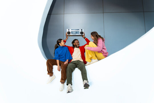 Friends dancing with boombox in retro style on white circle indoors