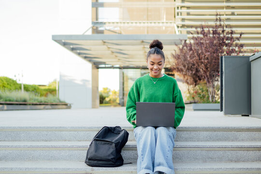 Student studying on outdoor campus stairs with laptop and backpack