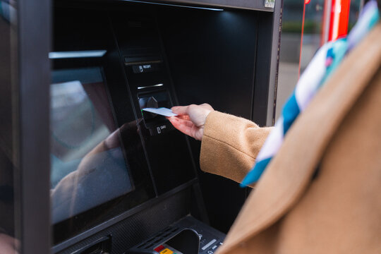 Hand inserting credit card into ATM for banking transaction outdoors