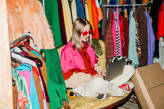 Entrepreneur working on laptop in colorful wardrobe selling clothes online