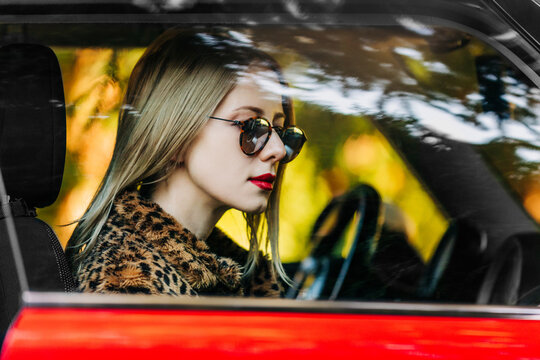 Fashionable woman in spotted fur coat driving retro car outdoors