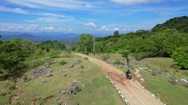Aerial drone footage of Fatumetan dirt road, with a trail motorbike passing by, and a huge wild valley behind, in Kupang regency, Timor island, Indonesia