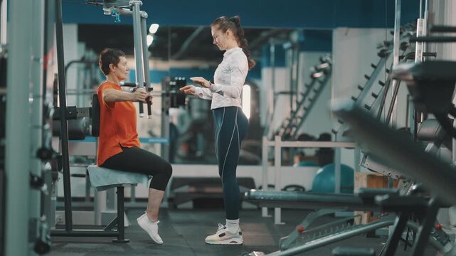 Personal trainer assisting senior woman on chest press machine