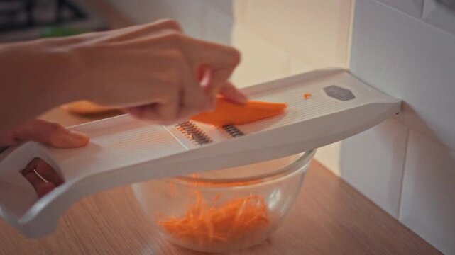 In a Korean kitchen, a cook uses a grater to slice carrots into thin strips, prepping them for a stir-fry. This technique showcases Korean cuisine&rsquo;s focus on texture and delicious flavor