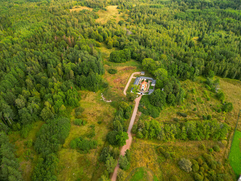 Traditional stone Orthodox skete on a hilltop surrounded by vast forest. High altitude aerial view of secluded monastery architecture.