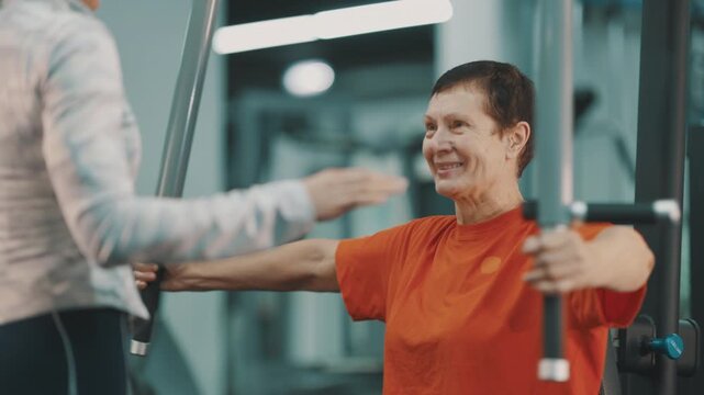Senior woman exercising on chest press machine with coach