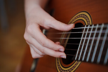 Fototapeta premium Person plays guitar with fingers on strings indoors in warm light
