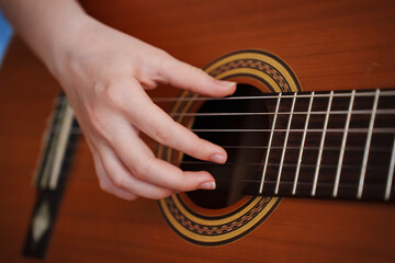 Fototapeta premium Girl plays guitar at home in afternoon with focus on hands