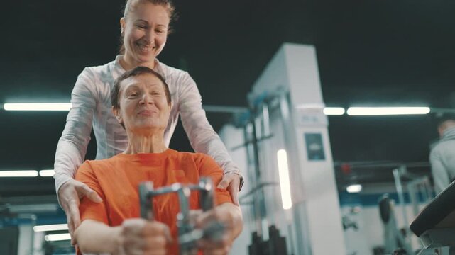 Personal trainer helping senior woman with seated cable row machine workout in a gym