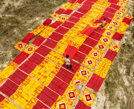 Narayanganj, Bangladesh - 30 March 2026: Aerial view of vibrant red and yellow textiles drying under the sun, creating a striking geometric pattern on the sandy ground.