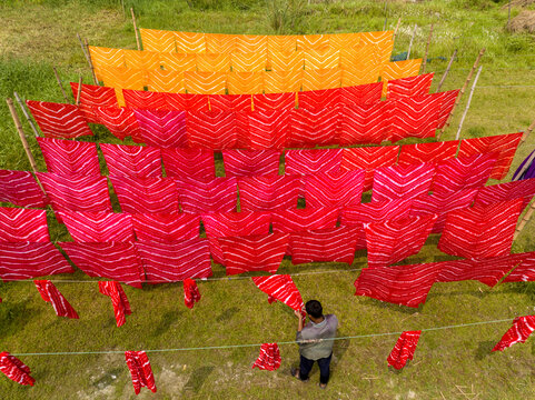 Narayanganj, Bangladesh - 30 March 2026: Aerial view of vibrant textiles displayed on bamboo frames, creating a striking contrast against the lush green field.