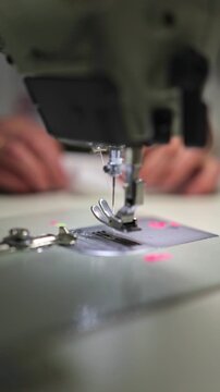 Detailed view of a professional sewing machine in motion. Metal needle rapidly stitching white textile material. Hands guiding fabric through the presser foot in a garment manufacturing plant.