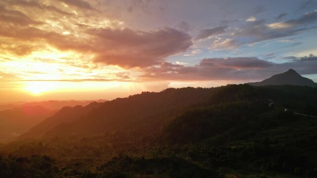 Aerial drone footage at sunset under the rain, of Timau mountain, with many mountains around, the ocean in the background, red sun, silhouettes, in Kupang regency, Timor island, Indonesia