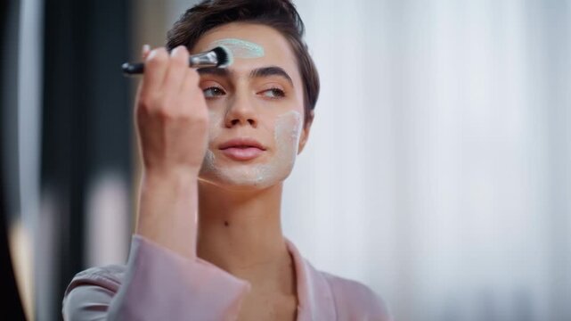 Morning woman applying clay mask healthy smooth face admiring reflection closeup