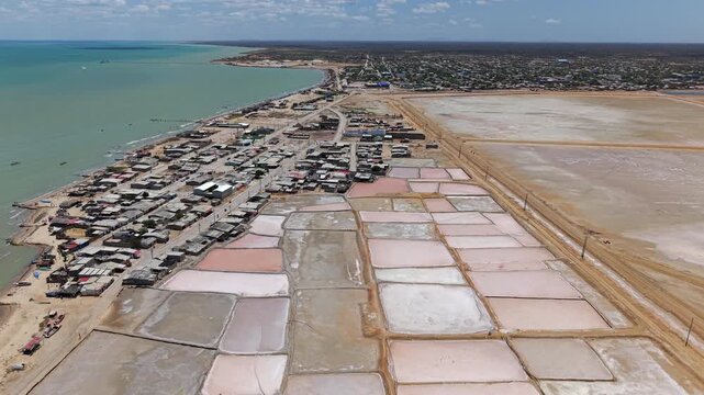 Drone footage captures the stunning salt flats of Manaure, Colombia. The aerial view showcases expansive salt pans against the blue Caribbean Sea, under a crisp, clear sky.