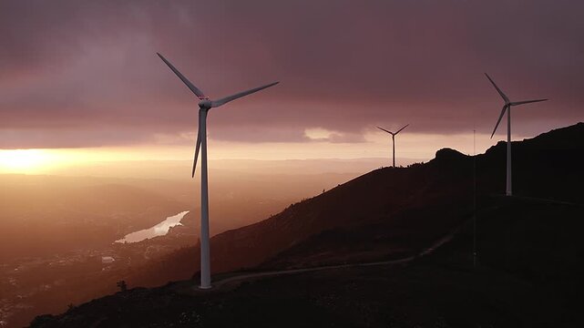 Group of wind turbines on Serra da Boneca in Penafiel Porto District Norte Portugal generating renewable energy along ridge with service road and Douro River valley under sunset light, drone pan