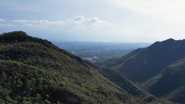 Margalla Hills frame Islamabad city with Faisal Mosque visible in the valley under hazy sky, Pakistan