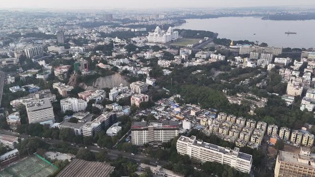 Wide cinematic aerial of Birla Mandir highlighting its elevated position on a green hill, intricate temple architecture, surrounding urban blocks, and the prominent Telangana State Secretariat