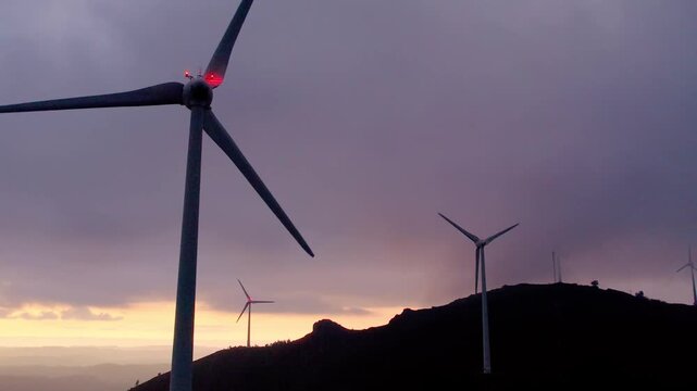 Wind turbine farm harnessing wind on Serra da Boneca in Penafiel Porto District Norte Portugal with visible nacelle and blades with aviation lights against cloudy sky, push in upward tilt shot
