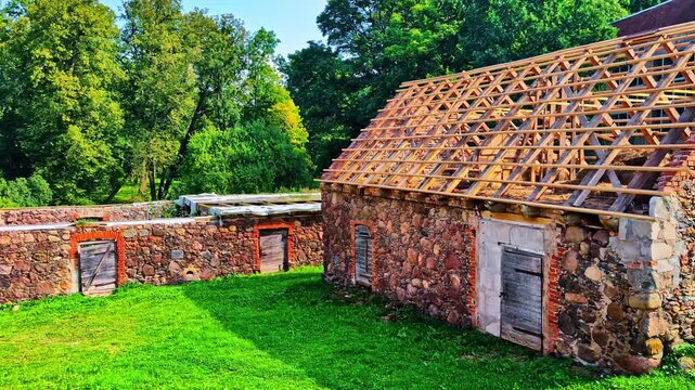 A cinematic pan across the rustic fieldstone walls and new wooden roof frame of a Latvian barn.