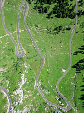 Aerial view of a serpentine road winding through verdant meadows and dark green forests, a contrast of man-made curves against nature's soft textures, Spiringen, Uri, Switzerland.