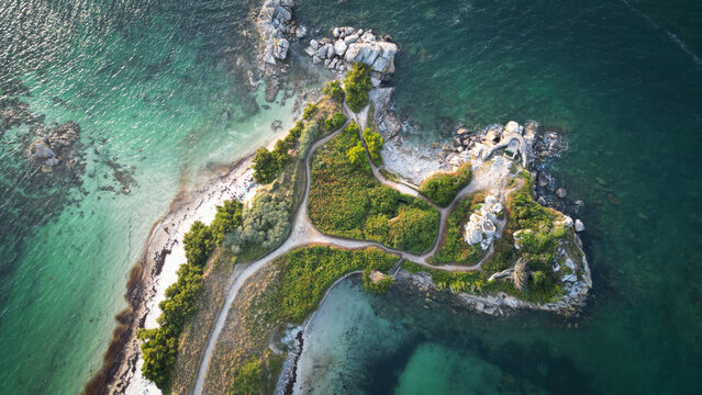 Aerial view of a small, rugged island with vibrant green vegetation contrasting against the turquoise waters, paths winding through the landscape, Roscoff, Finistere, France.
