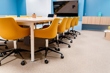 Naklejka premium A modern conference room with a long table surrounded by yellow upholstered office chairs with a professional atmosphere.