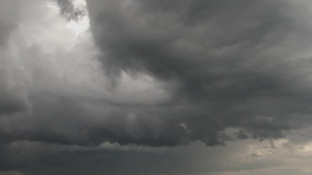 Dark storm clouds moving in semicircle formation across gloomy rainy sky.