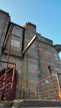 Aerial view of an old stone bridge with rusty metal chains and a red gate contrasts against the clear blue sky, Plouezoc'h, Bretagne, France.
