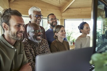 Fototapeta premium Business team smiling together at laptop in modern office collaborative workspace environment