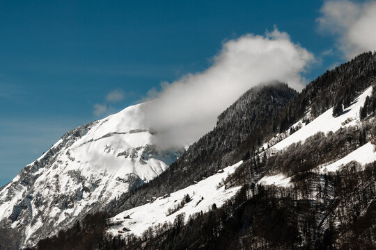 View of snow-dusted peaks rise against a clear blue sky, the cloud-veiled summits creating a stunning alpine panorama, Train from Lucerne to Interlaken, Switzerland.