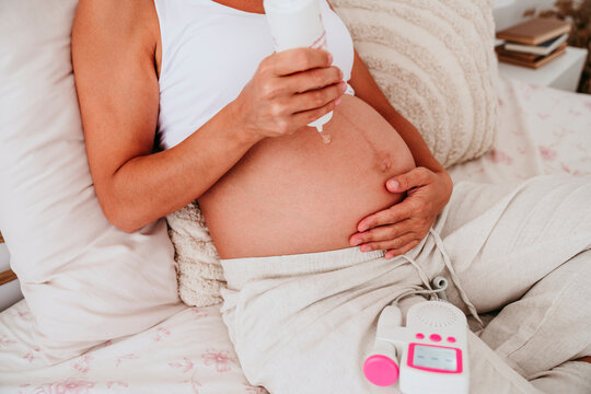 Pregnant person using doppler baby scan monitor at home