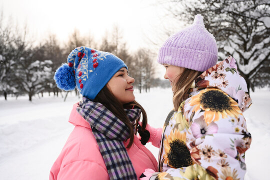 Mother and daughter in warm clothes embracing outdoors in winter