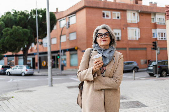 Woman walking outdoors with coffee on urban street in autumn