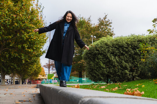 Smiling woman balancing on curb in city park on autumn day