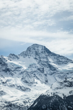 View of the crisp, snow-laden mountain peak rises against a backdrop of soft blue sky and wispy clouds, a scene of serene alpine beauty, Wengen, Switzerland.