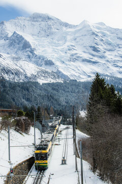 View of a train winding through a snow-covered landscape with towering, snow-capped mountains in the background, a scene of crisp air and serene beauty, Wengen, Switzerland.