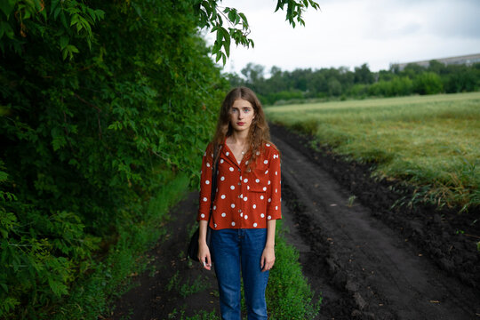 Woman with curly hair in red blouse standing in nature by a field