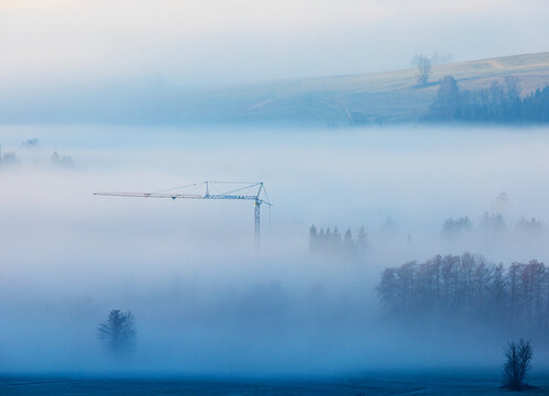 Construction crane and trees in early morning fog at Mondsee Austria