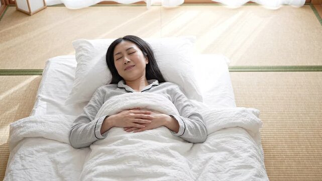 畳の部屋で布団に入り気持ちよさそうに眠る若い女性の俯瞰