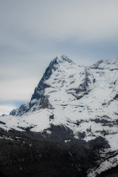 View of snow-capped mountain rises majestically against a cloudy sky, its rocky face partially covered in white, creating a stark contrast, Murren, Switzerland.