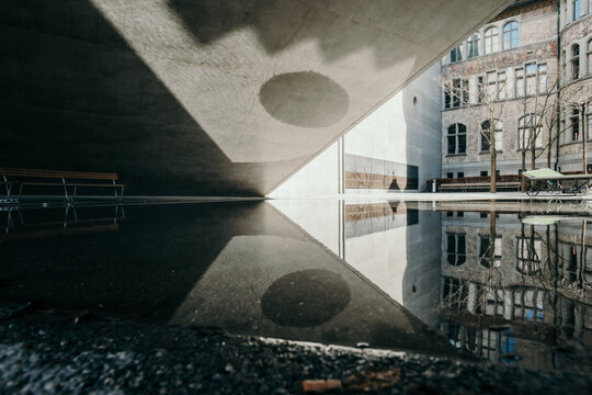 View of concrete architecture reflecting in a dark pool, where light and shadow dance in sharp contrast, creating a surreal urban landscape, Zurich, Switzerland.