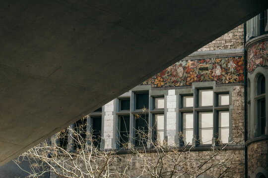 View of the detailed facade of the National Museum, with stone walls and colorful floral motifs, framed by a stark concrete structure above, Zurich, Switzerland.
