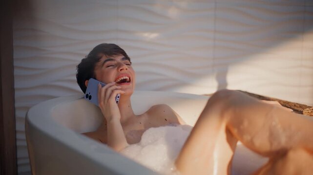 Laughing model talking smartphone in bathtub closeup. Happy girl lying hot bath