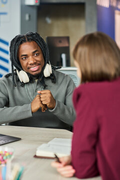Vertical shot of African American young man discussing ideas with colleague in office meeting, representing teamwork and communication. Useful for business coaching or HR content