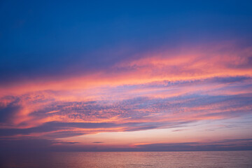 Fototapeta premium Orange and blue clouds in sunset sky over sea