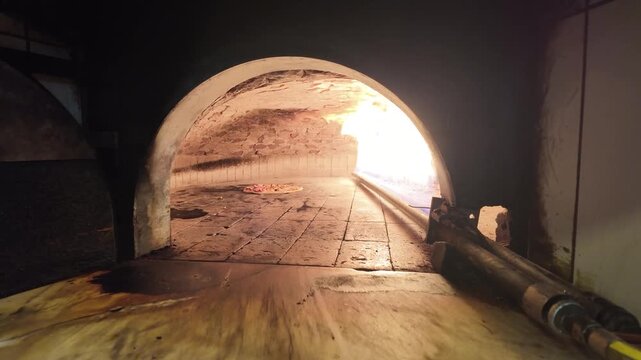 Traditional stone oven pizza baking with flickering flames inside a rustic wood-fired pizzeria furnace. Authentic Italian pizza cooking process in a professional restaurant kitchen with glowing fire.