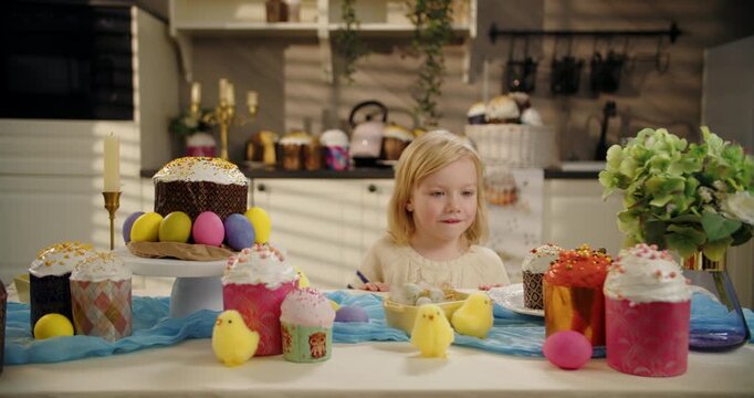 Little girl looking at Easter table with eggs and cake