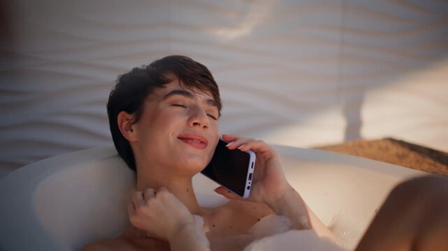 Bathing girl talking smartphone soaking fluffy bubbles closeup. Woman calling
